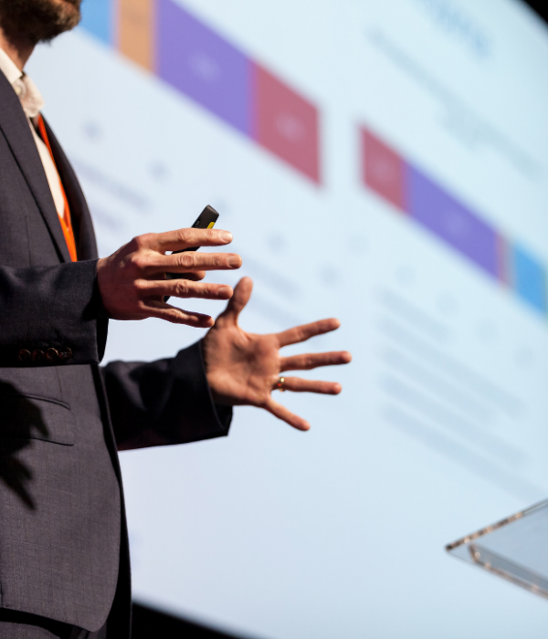 An image of a speaker at an event holding a remote control and using hand gestures.