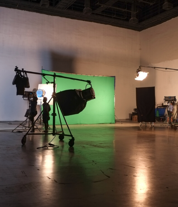 A big hall which has a green screen and other production equipment such as lights and cameras.