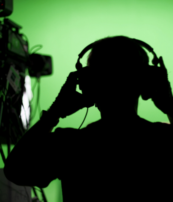 A shadowy man putting headphones on in front of a green screen.