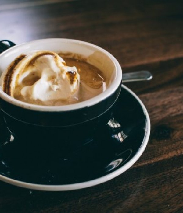 A coffee on a plate with a spoon, topped with whipped cream