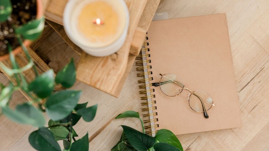 A candle and plant beside a notebook and some glasses