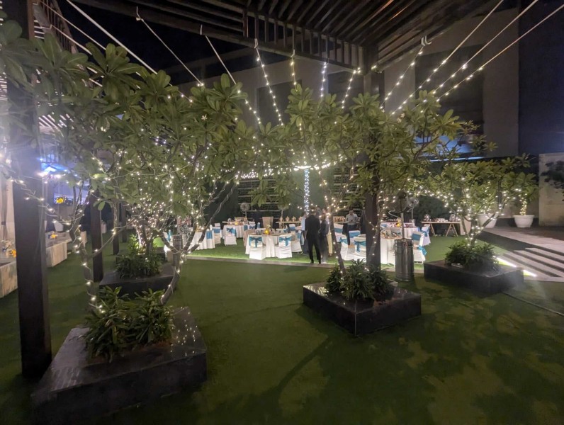 Decorative lighting hangs over a number of small trees in a university courtyard, where an evening meal is about to be served.